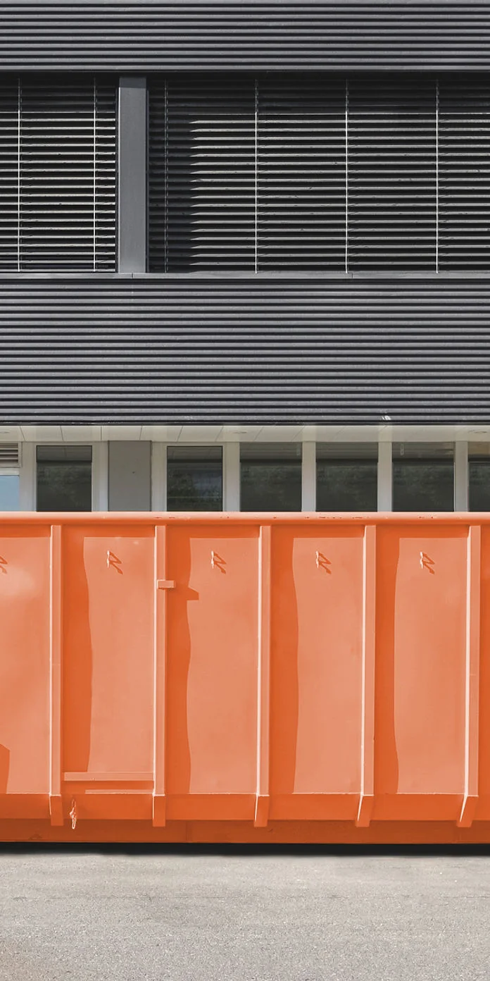 Oranžs metāllūžņu konteiners pie industriālas ēkas